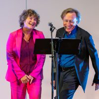 Gallery 3 - A woman and man standing at a music stand and microphone. 